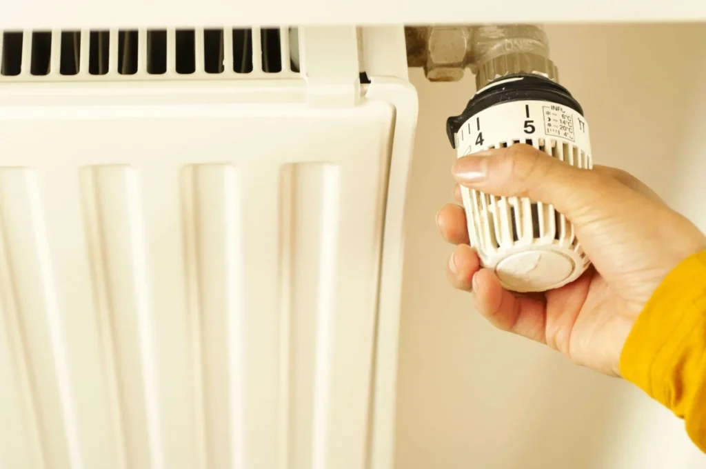 Hand stellt das Thermostat einer Heizung ein – der hydraulische Abgleich zählt zu den förderfähigen Umfeldmaßnahmen der Heizungsförderung 458